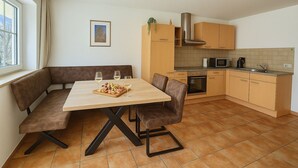 A compact kitchen with a dining area, featuring a wooden table, brown upholstered chairs, and a small countertop with a microwave and kettle. - Stylish mountain apartment with terrace in Flattach near Mölltal Glacier (Flattach)