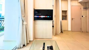 A modern hotel room with a large flat-screen TV mounted on a wall, a glass table with a remote control, and a sliding door leading to a balcony. - Resort Living at Great Location (Pattaya)