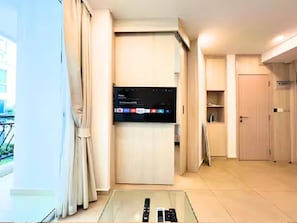 A modern hotel room with a large flat-screen TV mounted on a wall, a glass table with a remote control, and a sliding door leading to a balcony. - Resort Living at Great Location (Pattaya)