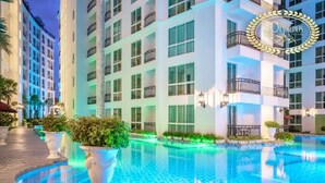 A hotel with a swimming pool, large windows, and a well-lit exterior. - Resort Living at Great Location (Pattaya)