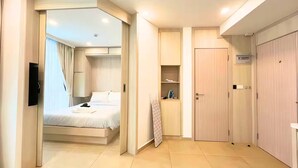 A hotel room with a bed, a TV mounted on the wall, a wardrobe, and a small shelf with items. - Resort Living at Great Location (Pattaya)