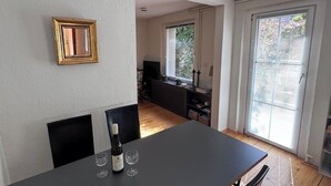 A dining area with a table, chairs, and a bottle of wine. There is a window with blinds and a view of greenery outside. - Small house | city location | seeglueck (Konstanz)