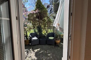 Une terrasse extérieure avec deux fauteuils en osier, une petite table et des plantes en pot.