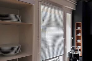A kitchen with white cabinets, a coffee machine, and a window with blinds.