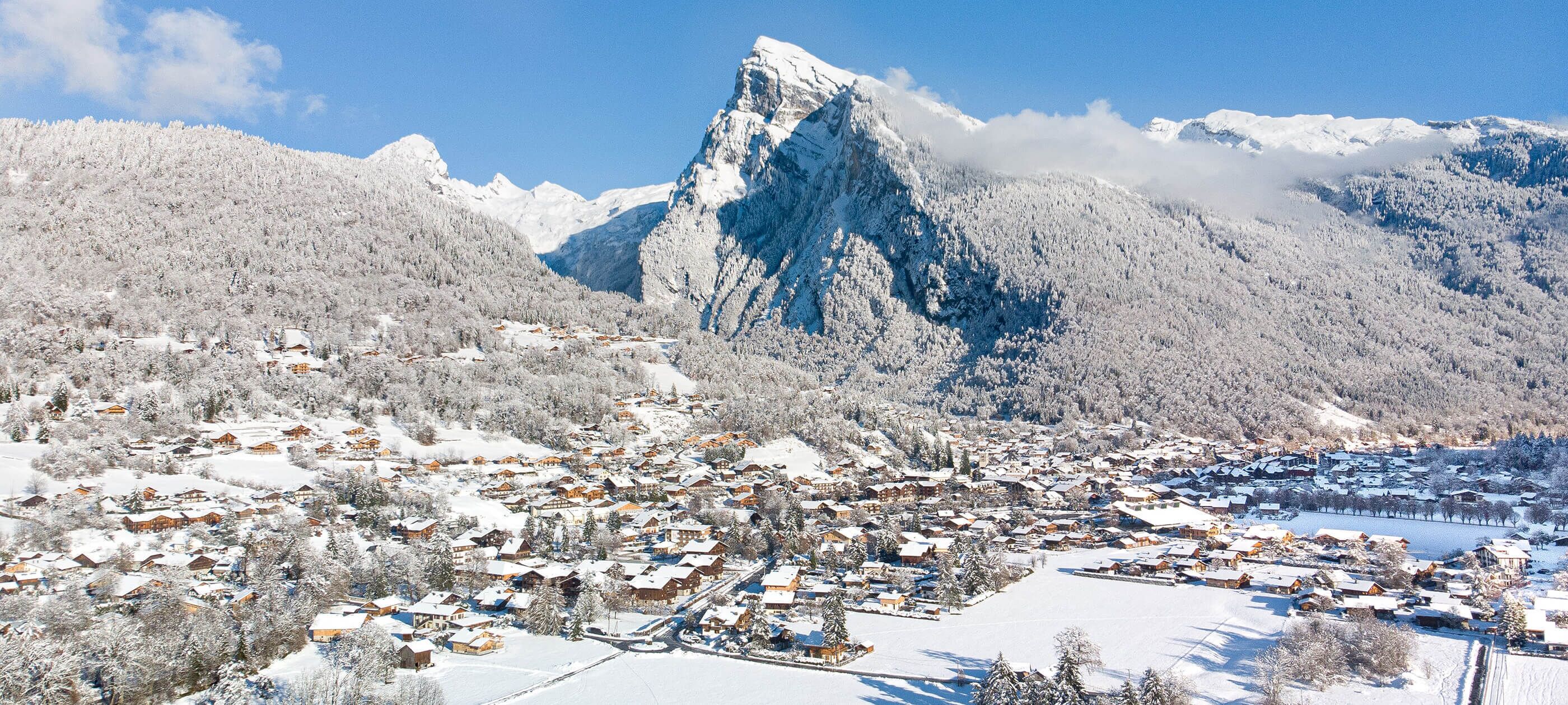 A snow-covered village with houses and a prominent mountain peak in the background.