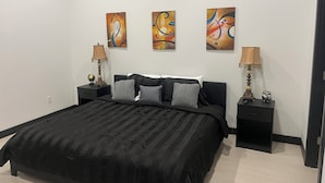 Een slaapkamer met een zwart bed, twee nachtkastjes en drie abstracte schilderijen aan de muur.