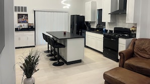 Een moderne keuken met een centraal eiland, zwarte apparaten, witte kasten en een hangende lamp.
