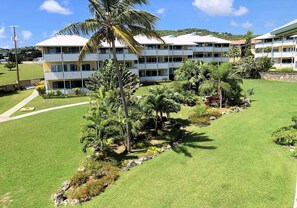 Ein mehrstöckiges Hotel mit Balkonen, umgeben von gepflegten Rasenflächen und Palmen.