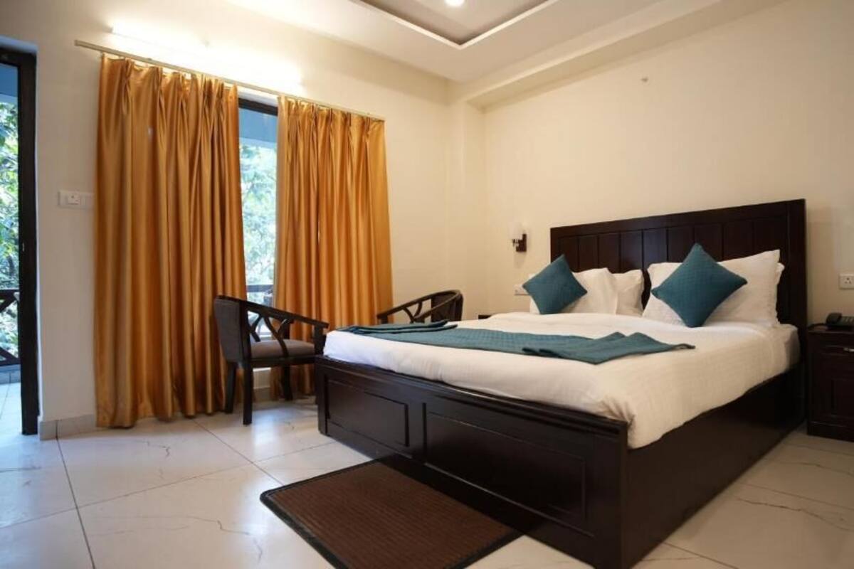 A bedroom with a large bed, a chair, a nightstand, and a view of the outdoors through curtains.