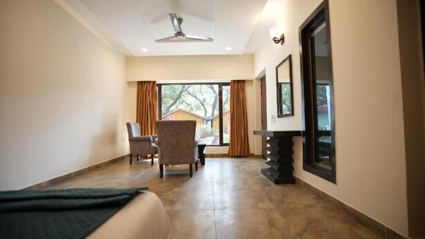 A hotel room with a bed, a chair, a desk, a window with curtains, and a ceiling fan. - Wild Vista Corbett Resort (Dhikuli)