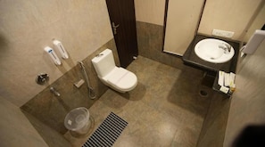 Een kleine badkamer met toilet, wastafel en douche. Er zijn handdrogers en een prullenbak.