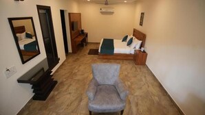A hotel room with a bed, a chair, a desk, a mirror, and a ceiling fan. - Wild Vista Corbett Resort (Dhikuli)