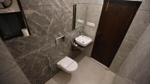 A bathroom with a dark marble wall, a white sink, a toilet, and a dark wooden door. - Wild Vista Corbett Resort (Dhikuli)