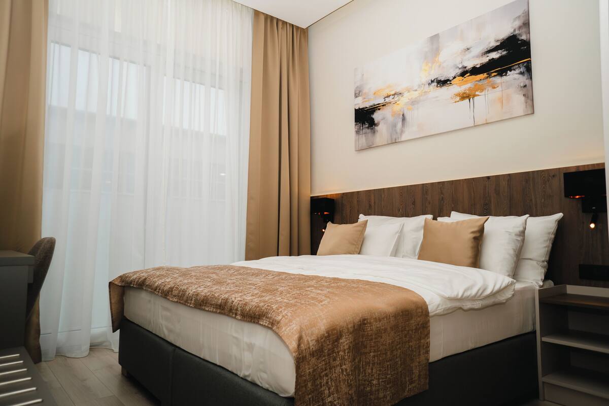 Una habitación de hotel moderna con una cama grande, un escritorio y una ventana con cortinas translúcidas.