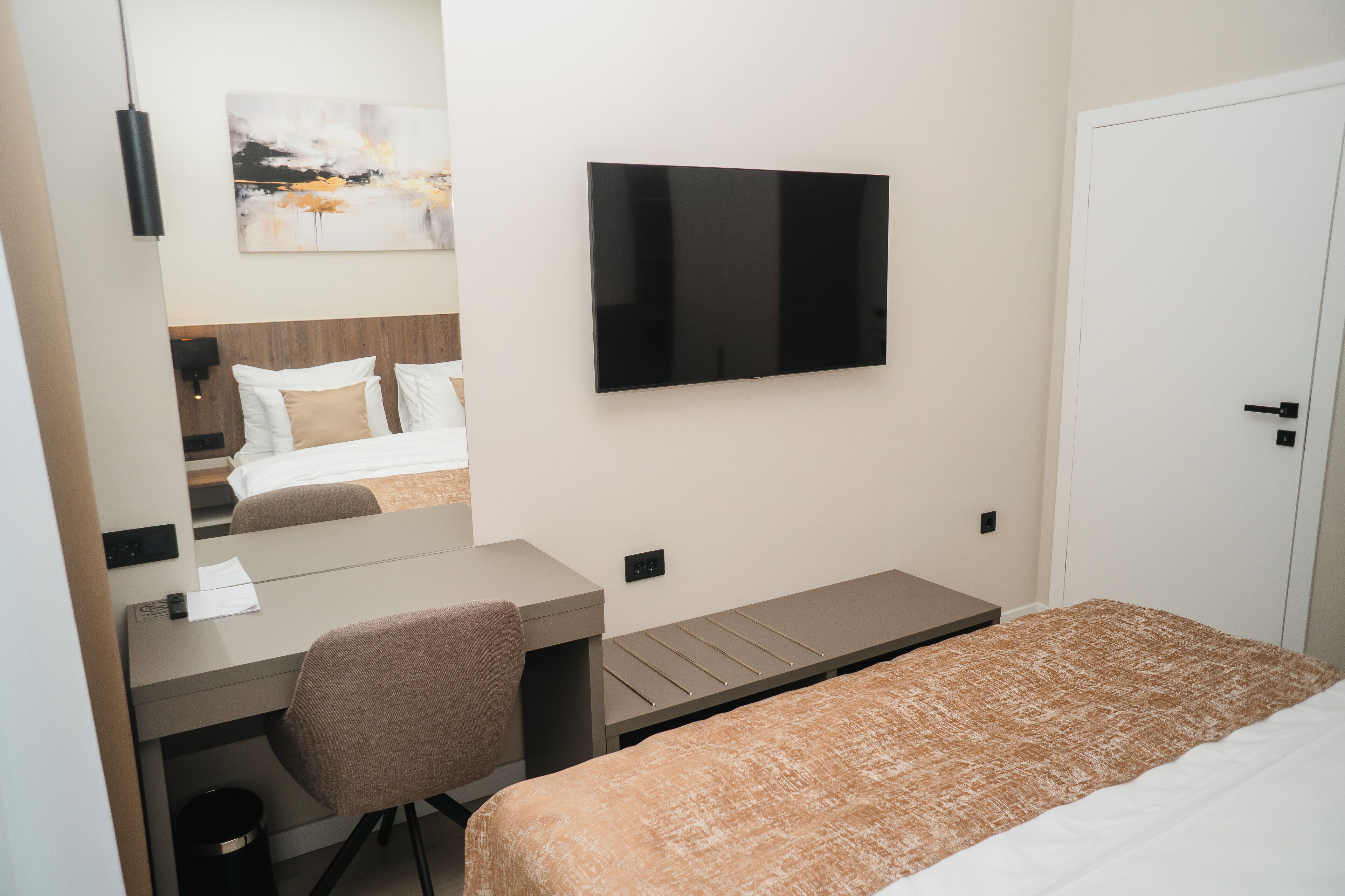 A hotel room with a bed, a desk, a chair, a TV mounted on the wall, and a door.