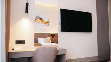 Une chambre d’hôtel équipée d’un lit, d’un bureau, d’une chaise, d’un téléviseur à écran plat et d’une œuvre d’art accrochée au mur.