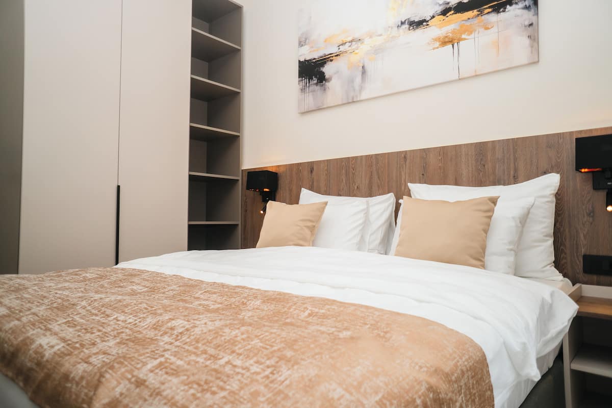 Un dormitorio moderno con cabecera de madera, una cama grande con ropa de cama blanca y beige, y estantes empotrados a la izquierda.