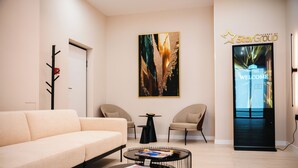A modern hotel lobby with a sofa, two chairs, a coffee table, a wall art piece, and a StarGroup welcome screen. - Stars Hotel (Jelah)