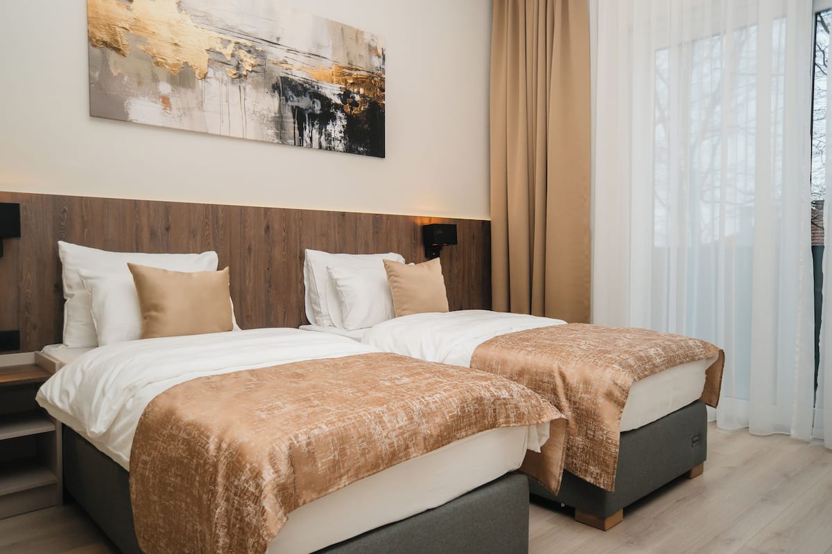 Habitación de hotel con dos camas, cabecero de madera, un cuadro abstracto grande y cortinas de gasa.