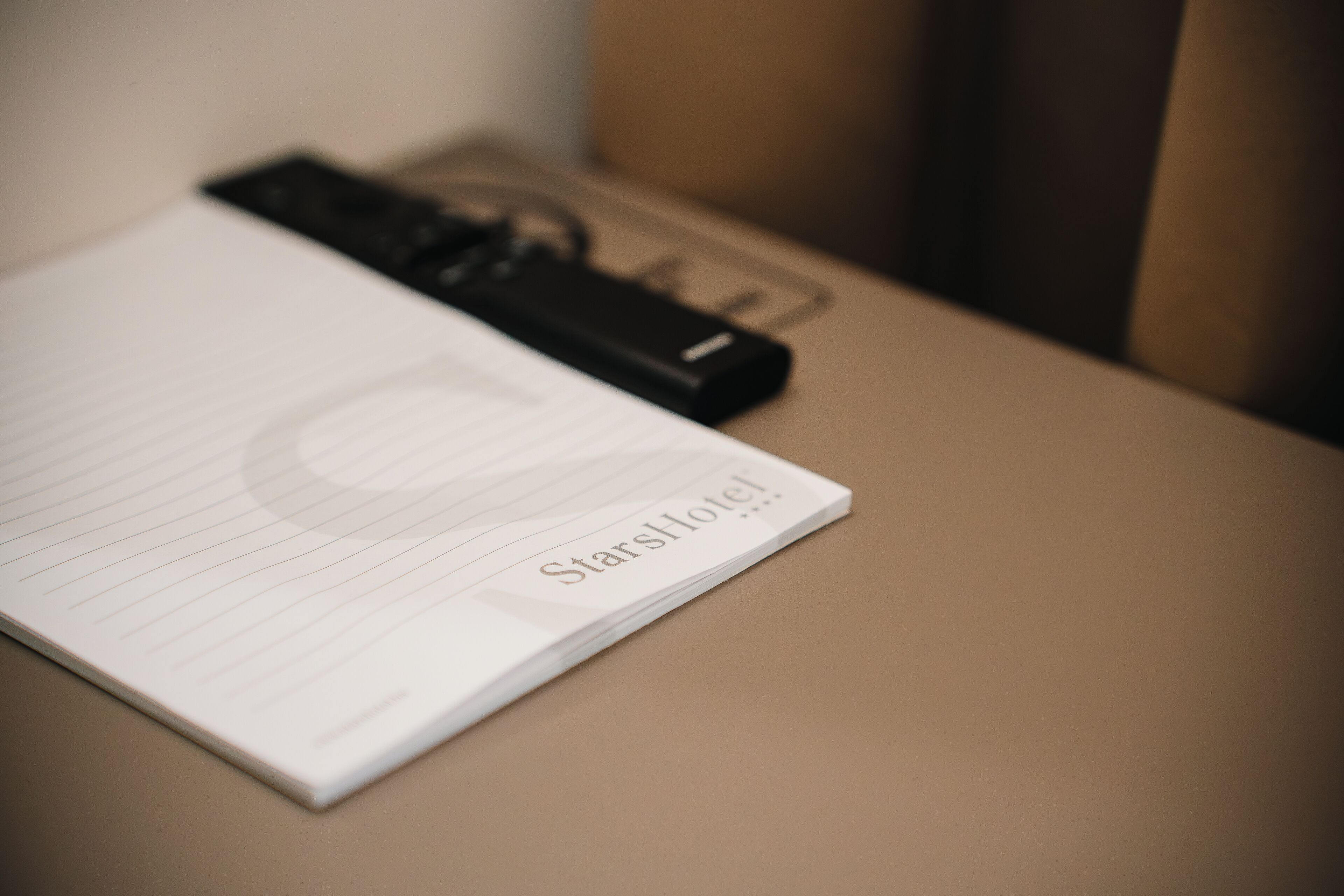 Um caderno com o texto "StarsHotel", colocado sobre uma mesa ao lado de um objeto preto.