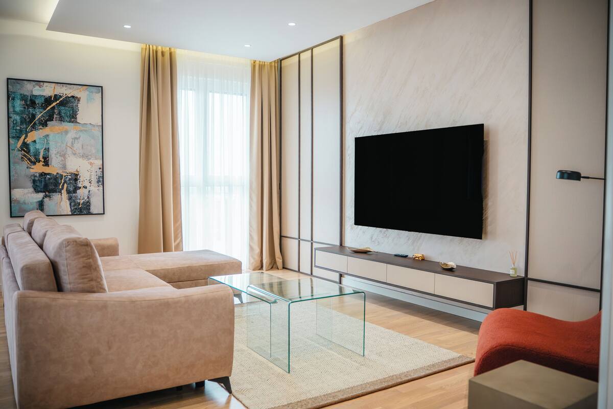 Un salón moderno con un sofá beige, una mesa de centro de vidrio y un televisor de pantalla plana montado en la pared.