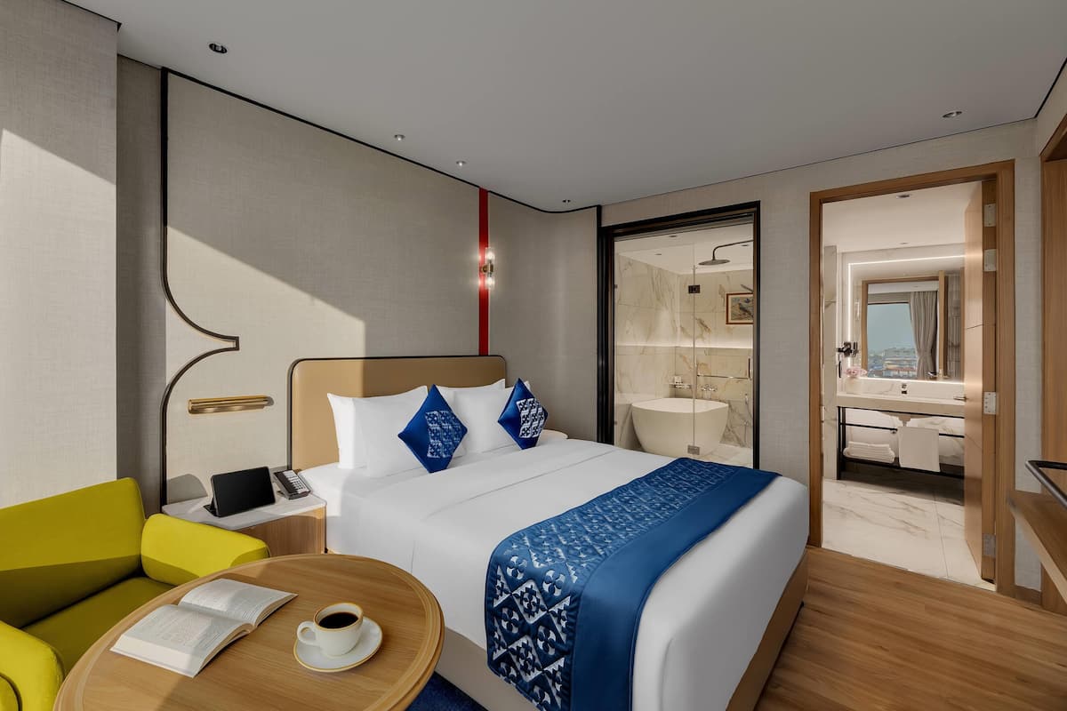 Une chambre d’hôtel moderne équipée d’un lit, d’une table de chevet, d’une lampe et offrant une vue sur la salle de bain.