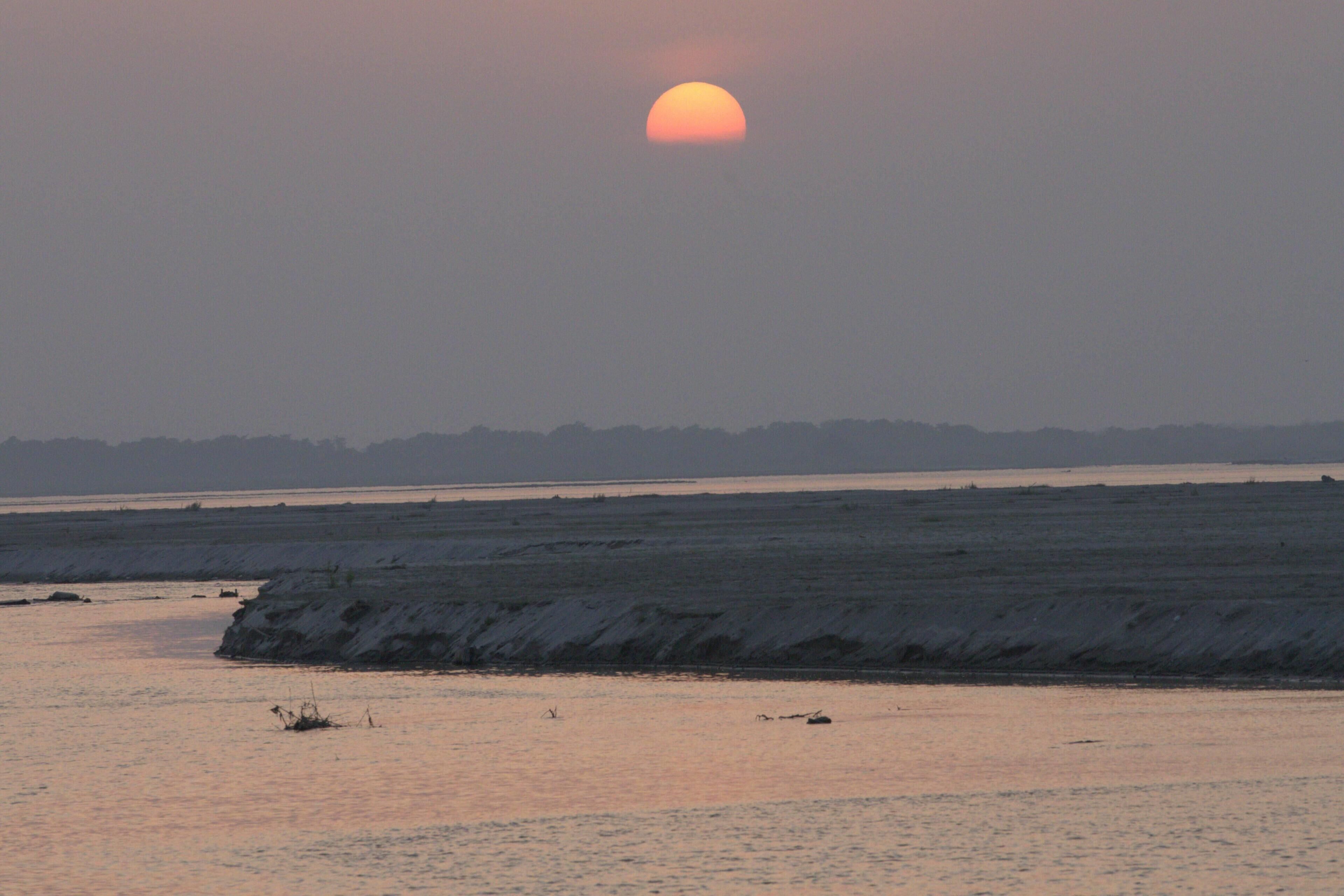 A sunset over a calm body of water with a distant shoreline.