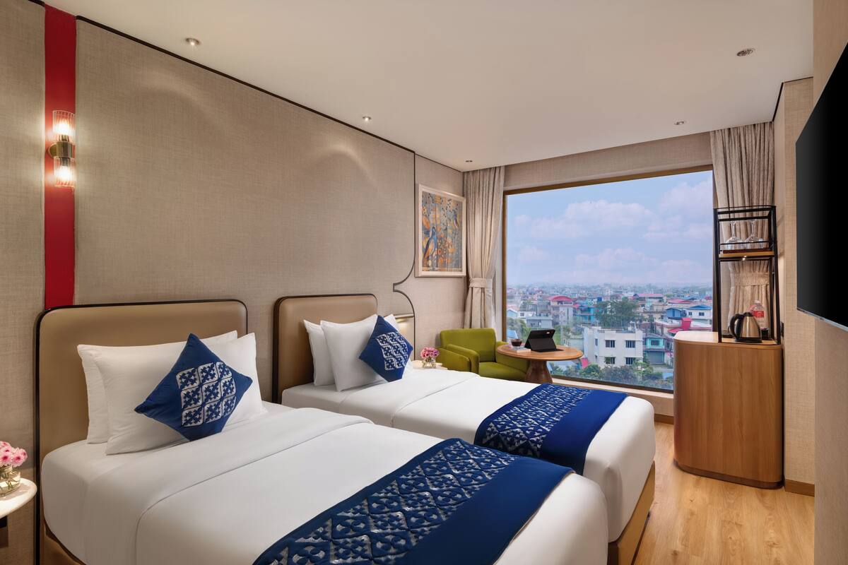 Une chambre d’hôtel avec deux lits, un bureau, une chaise, une télévision et une fenêtre donnant sur la ville.