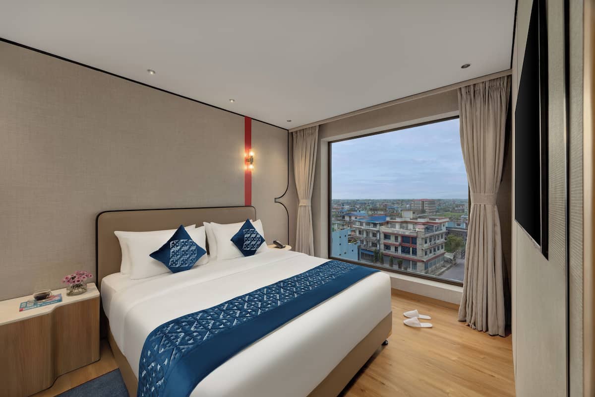 Une chambre d’hôtel moderne avec un grand lit, une table de chevet, une télévision et une vue sur la ville.