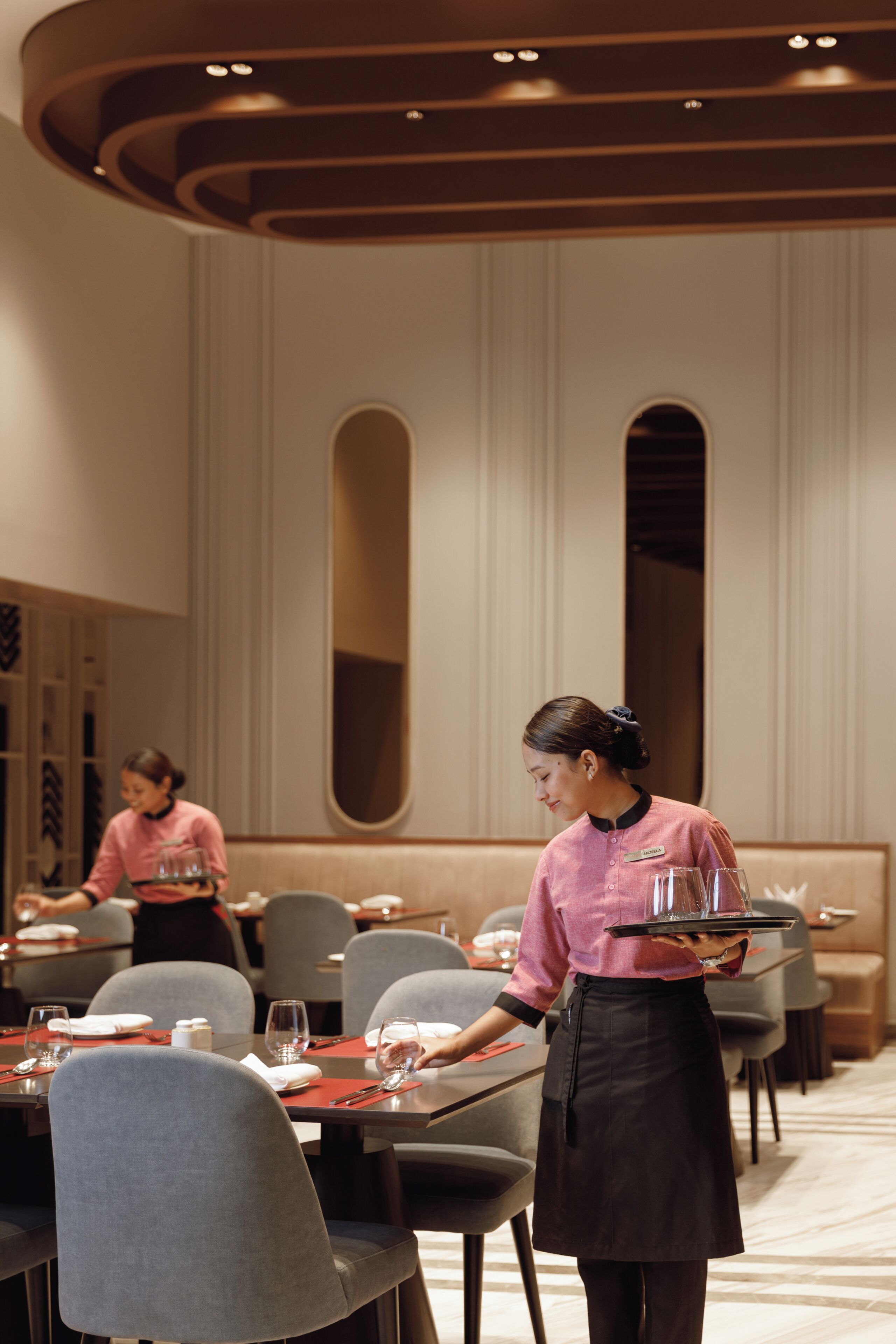 A restaurant with tables set for dining, a waiter serving a tray, and a modern interior design.