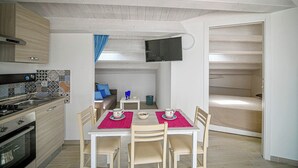 Une cuisine compacte avec un coin repas, un téléviseur fixé au mur et un lit dans la pièce adjacente.