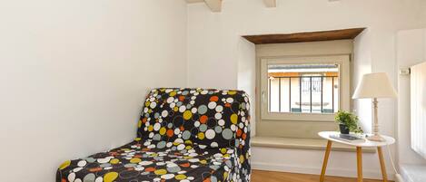 A small room with a polka-dotted sofa, a small table with a lamp, and a window with a view.