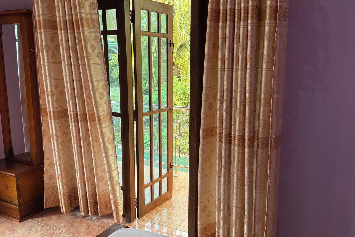 A bedroom with a bed, white towels, and a view of a balcony with greenery.