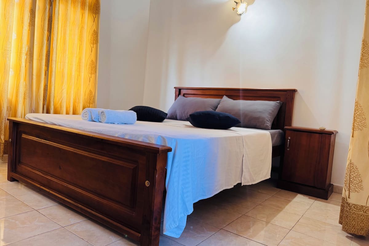 A neatly made bed with a wooden headboard, a bedside table, and a wall-mounted light fixture.