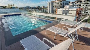 A rooftop pool area with lounge chairs and a view of modern buildings.