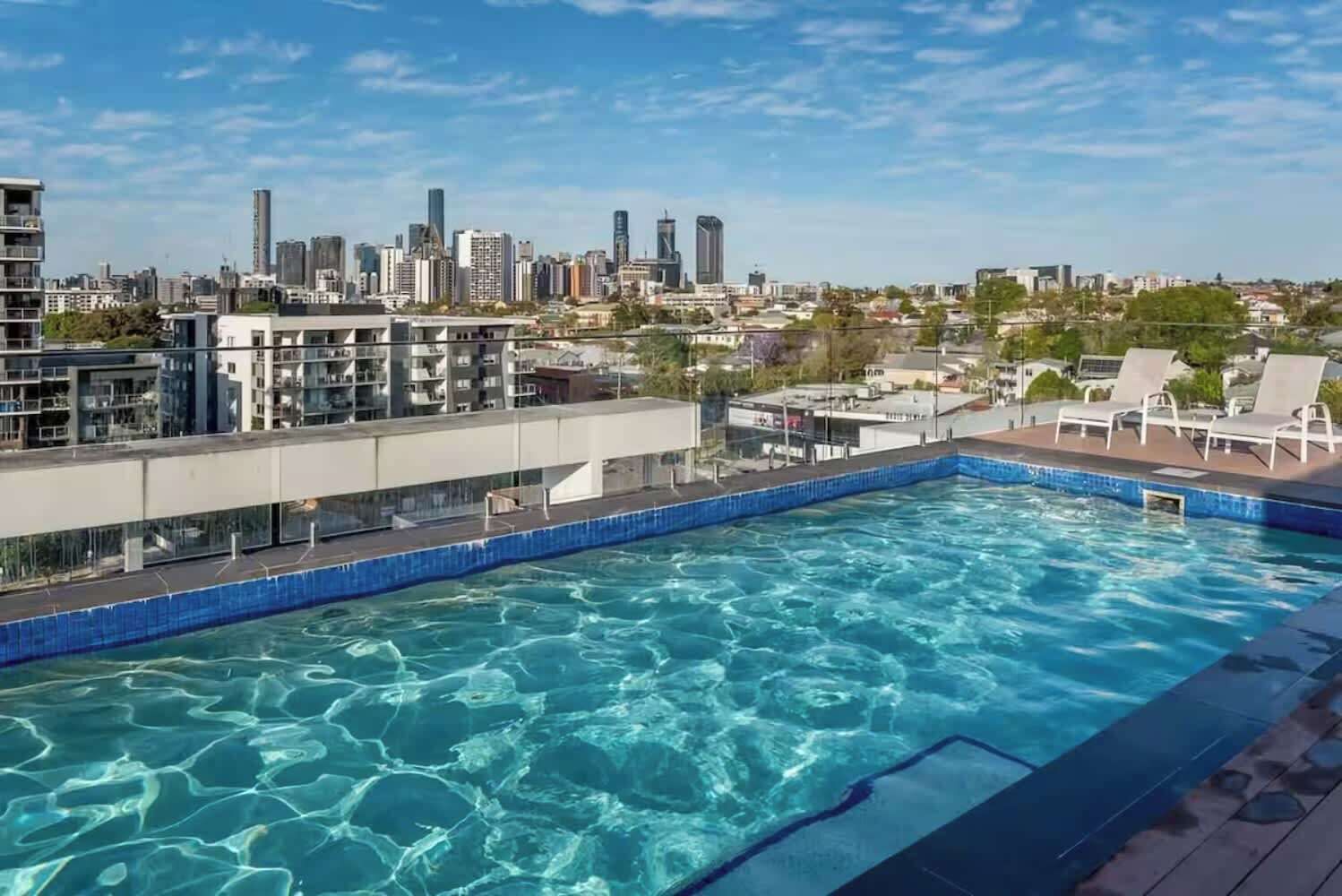 Une piscine sur le toit, avec une eau d’un bleu cristallin, entourée de bâtiments modernes et offrant en arrière-plan une vue sur les gratte-ciel de la ville.