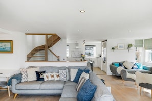 A spacious living area with a grey sectional sofa, a grey armchair, and a wooden staircase. - Little Harbour Master's House is a beautifully presented home set on the harbour (Portreath)