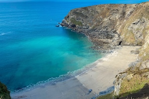 Paisagem costeira com uma praia, águas turquesa cristalinas e falésias rochosas.