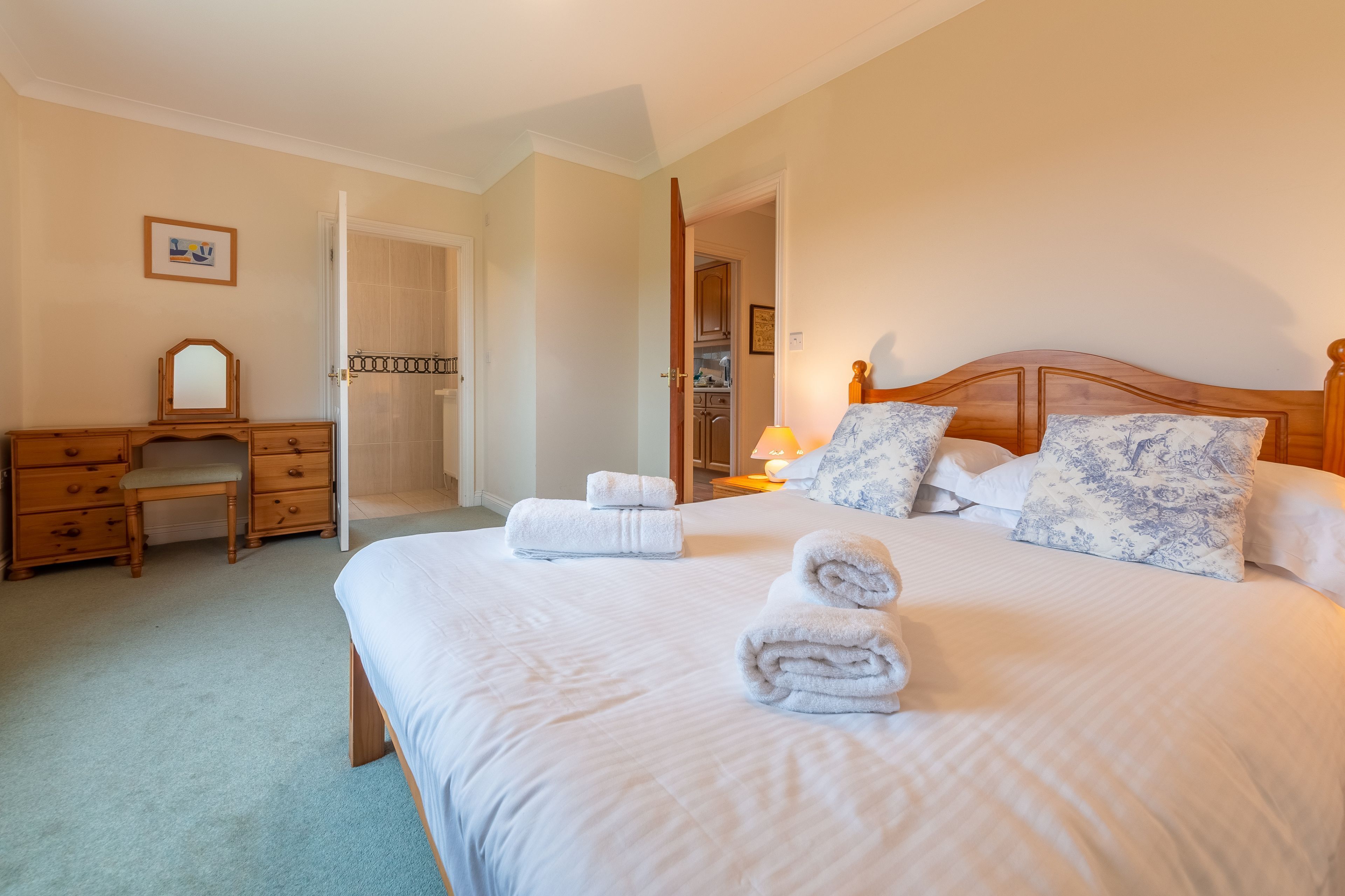 A bedroom with a large bed, a wooden dresser, a desk, and a chair.