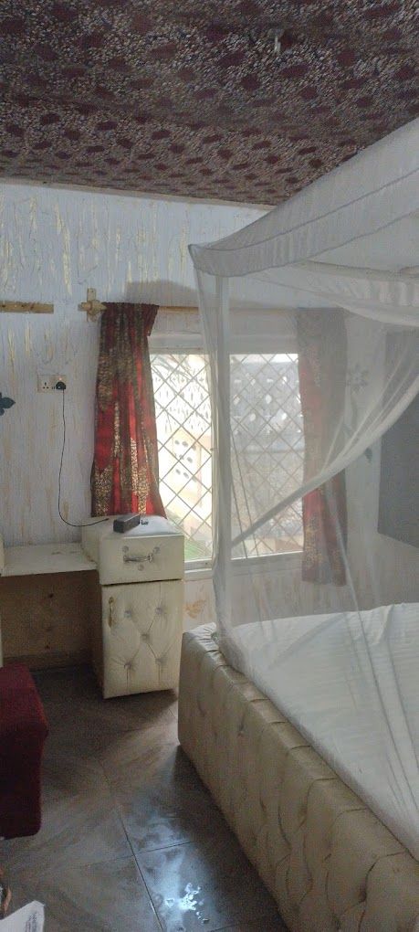 A bedroom with a bed, a nightstand, a window with curtains, and a patterned ceiling.