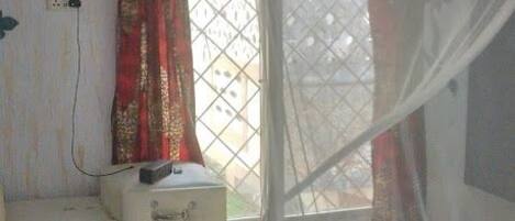 A bedroom with a bed, a nightstand, a window with curtains, and a patterned ceiling.