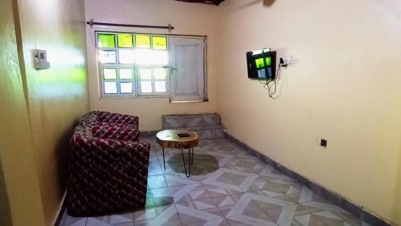 Una habitación pequeña y estrecha con suelo estampado, un sofá, una pequeña mesa redonda, una ventana con vistas y un televisor montado en la pared.