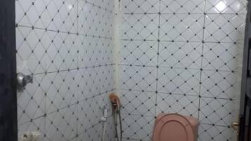 Un baño pequeño con inodoro rosa, paredes de azulejos blancos y zona de ducha.
