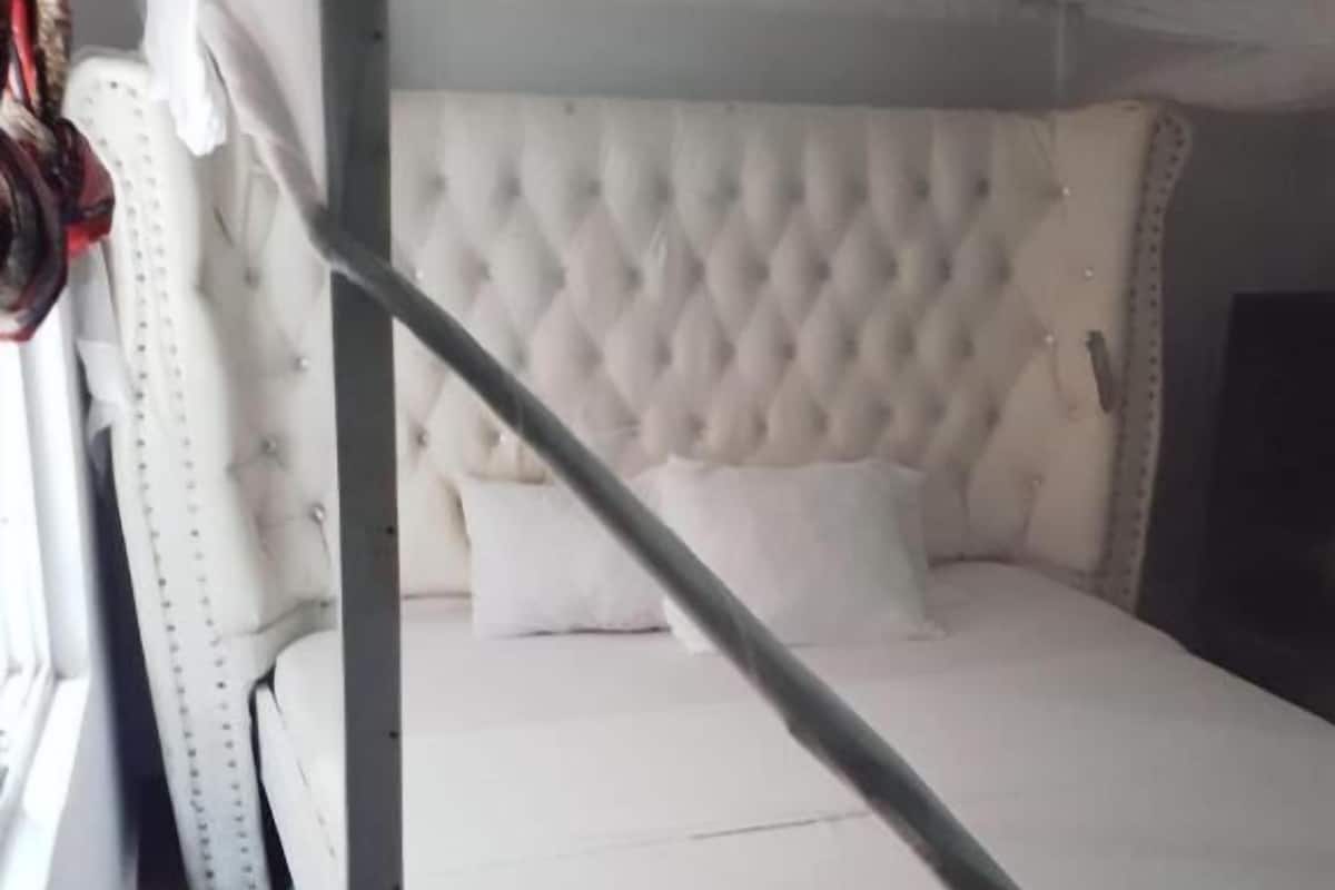 Een bed met een gestoffeerd hoofdeinde, een raam met gordijnen, en een witte muur.