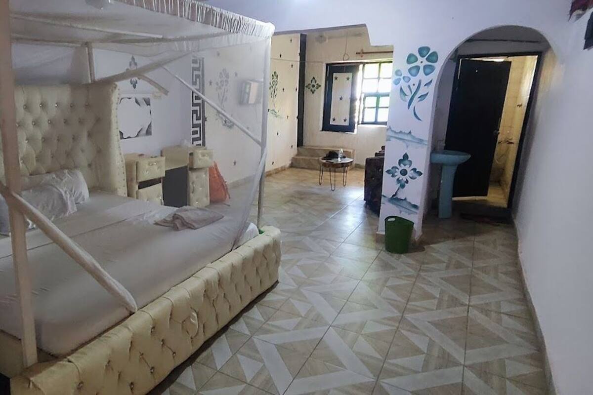 Een slaapkamer met een hemelbed, een klein tafeltje en een stoel.