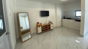 A modern hotel room with a large mirror, a flat-screen TV, a wooden console, and a kitchenette. - Ha Nguyen's House (Hue)