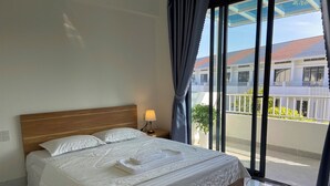 A hotel room with a large bed, a nightstand with a lamp, and a view of the outside balcony. - Ha Nguyen's House (Hue)
