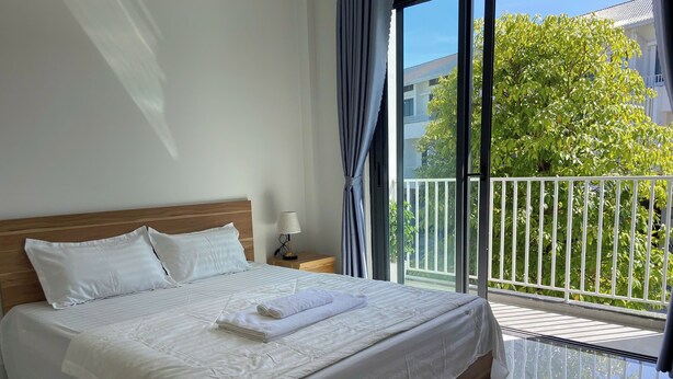 A neatly made bed with white linens, a wooden headboard, and a nightstand with a lamp. - Ha Nguyen's House (Hue)