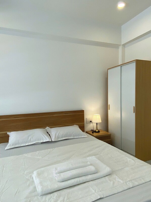A hotel room with a bed, a nightstand with a lamp, and a wardrobe. - Ha Nguyen's House (Hue)