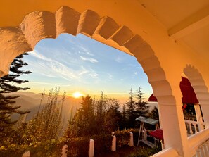 A view through an arched doorway overlooking a mountainous landscape with a sunset. - Himalayan Retreat Neelkanth (aalukhet)